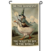 Decorative garden flag with a cartoon owl in a wizard hat riding a goose, featuring text 'Be the nonsense you want to see in the world'.