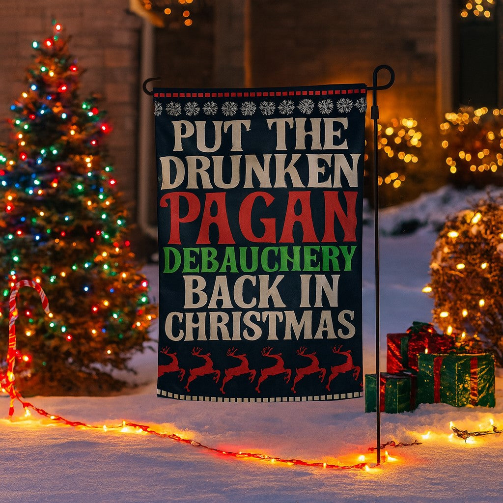 Christmas-themed garden flag with humorous text in front of a decorated Christmas tree and lights.
