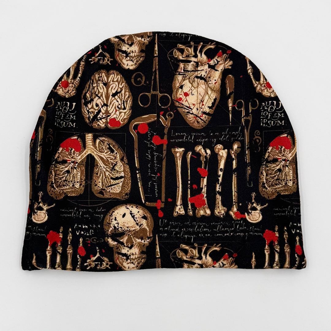 Beanie with anatomical design featuring skulls, bones, and medical tools on a black background.