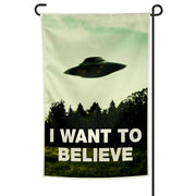 A garden flag with the phrase 'I WANT TO BELIEVE' printed on it, featuring a silhouette of a flying saucer above a tree line.