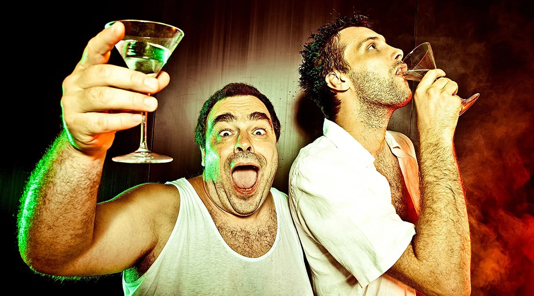 Two men drinking from glasses with a dark, smoky background